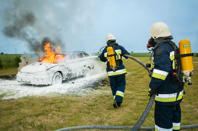 Firefighters spray on a burning car